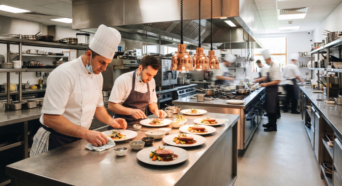 Chefs plating dishes in a spotless, professional restaurant kitchen operating under pristine sanitary conditions.